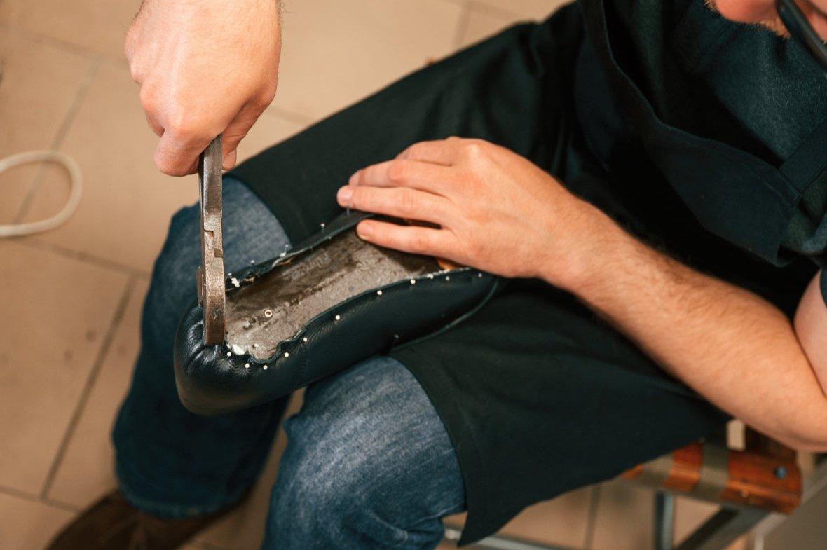 L'uomo tira concentrato la pelle tesa sopra il forma della scarpa e la fissa con chiodi.