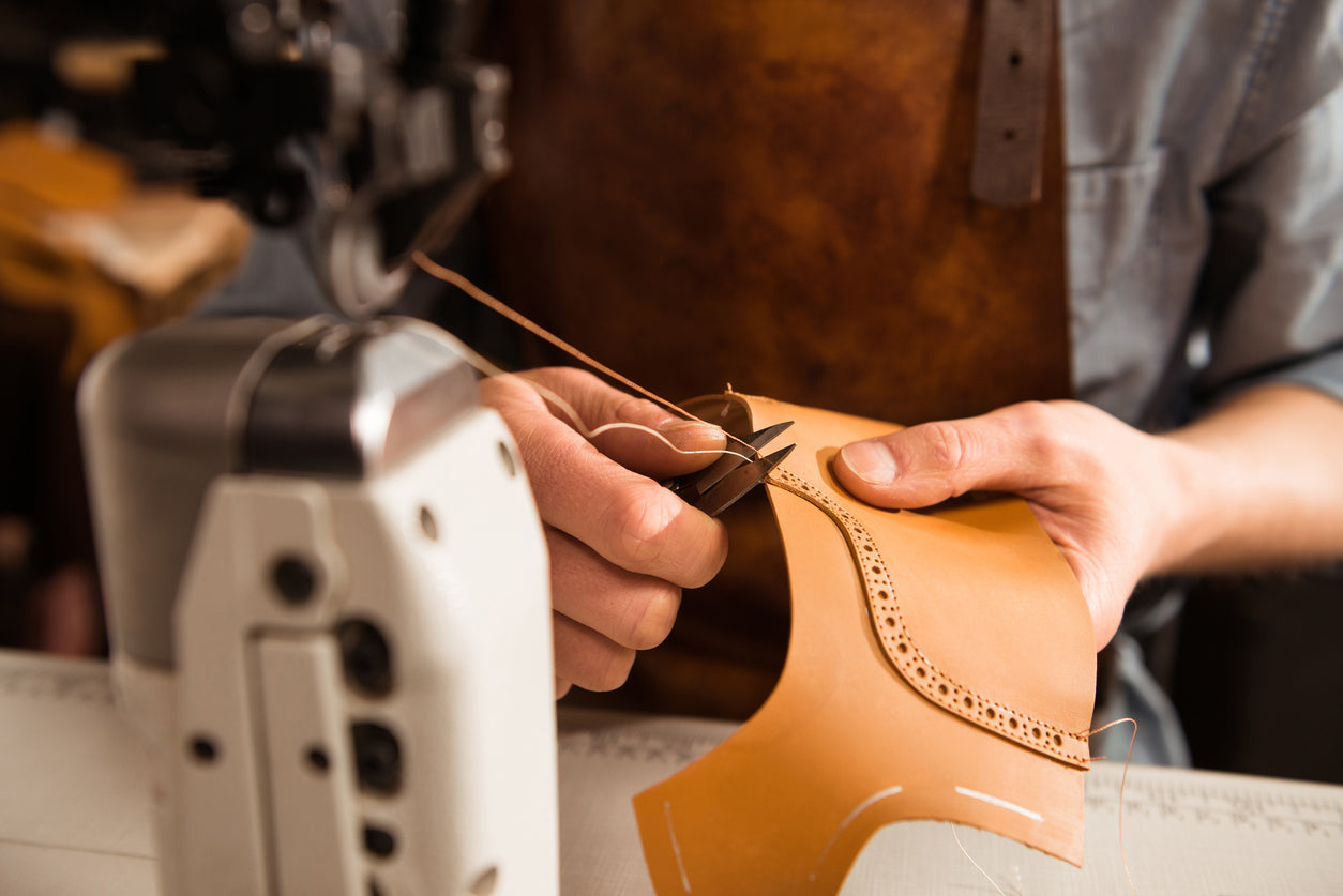 Artigiano mentre cuce a mano dettagli in pelle per scarpe italiane di lusso, simbolo di qualità e tradizione firmato Poiché Milano.