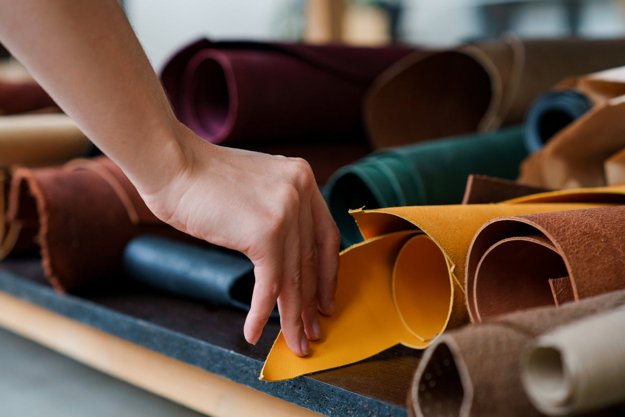 Mano che seleziona pregiati rotoli di pelle per la creazione di scarpe italiane di lusso, espressione della qualità artigianale firmato Poiché Milano.