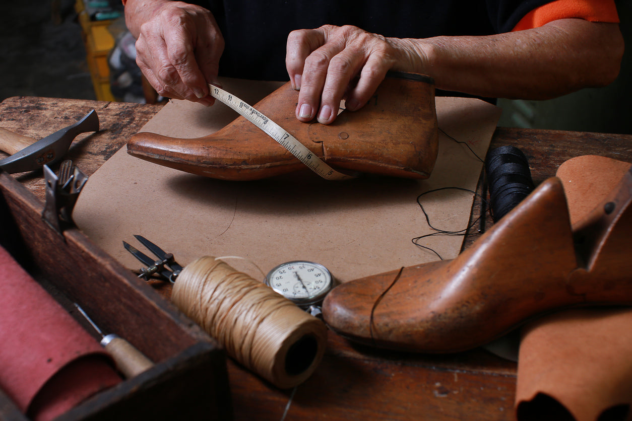 Artigiano che misura una forma in legno per scarpe italiane su misura, circondato da strumenti tradizionali, simbolo di qualità e precisione firmato Poiché Milano.