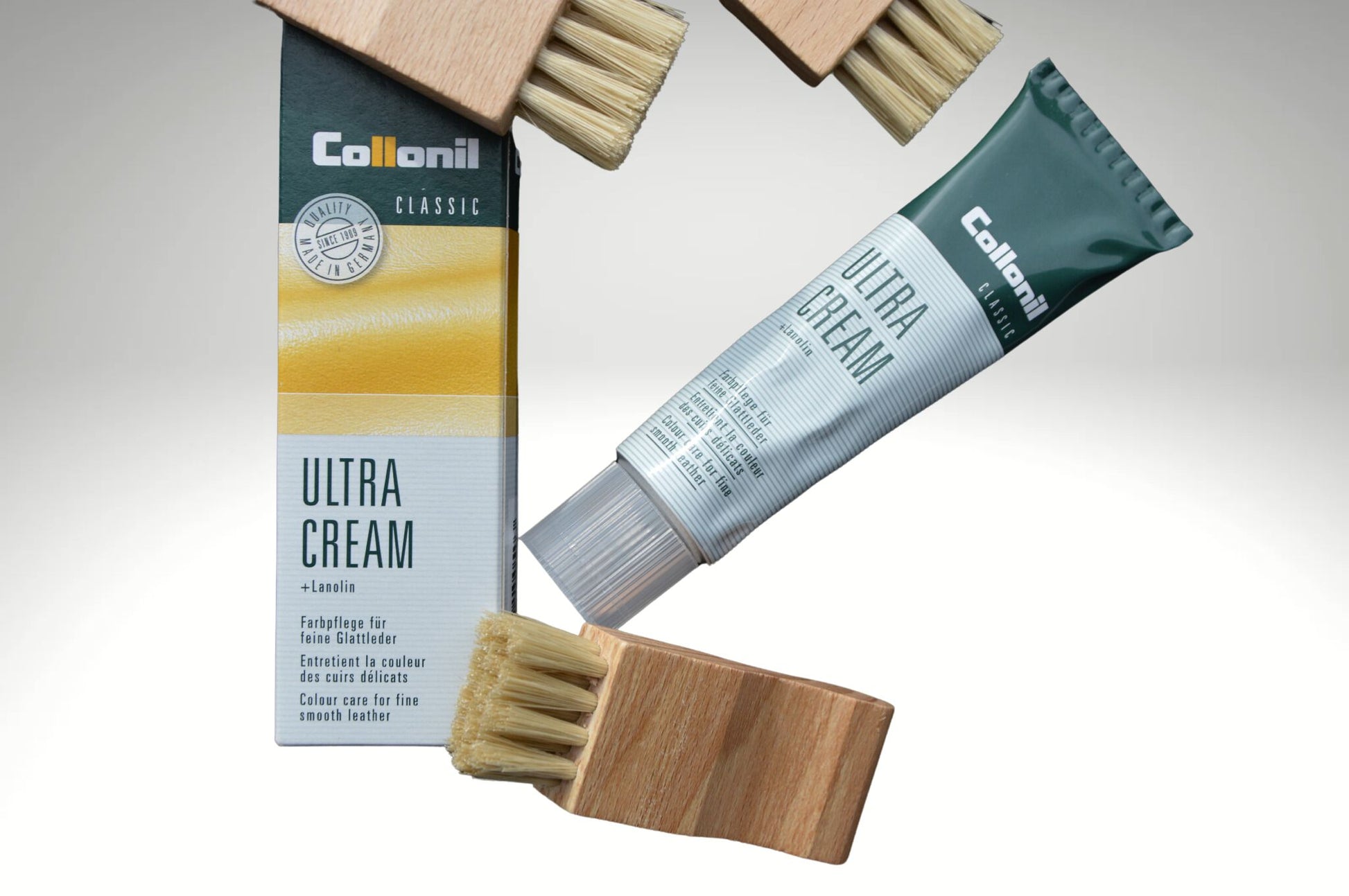 Sfondo bianco con un delicato sfumatura di colore, con una confezione di Collonil Ultra Cream in tubo, un cartone e tre spazzole per applicazione marchiate Poiché Milano.